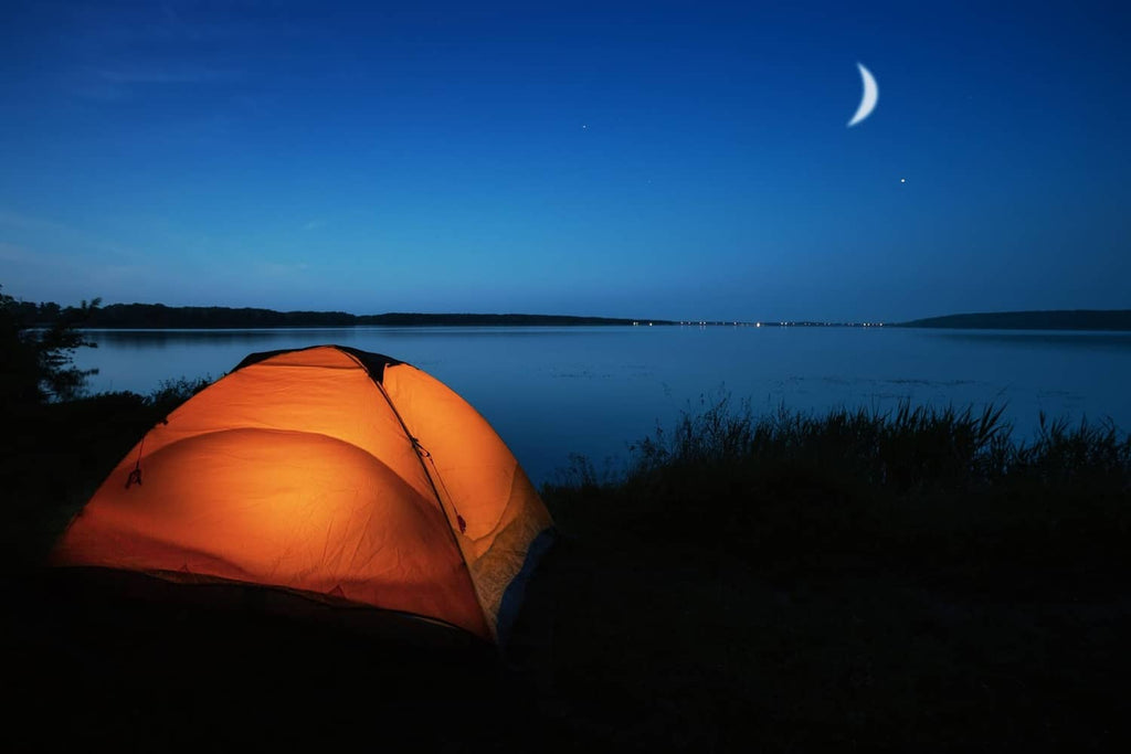 Orange camping tent illuminated by focused flashlight beam at dusk