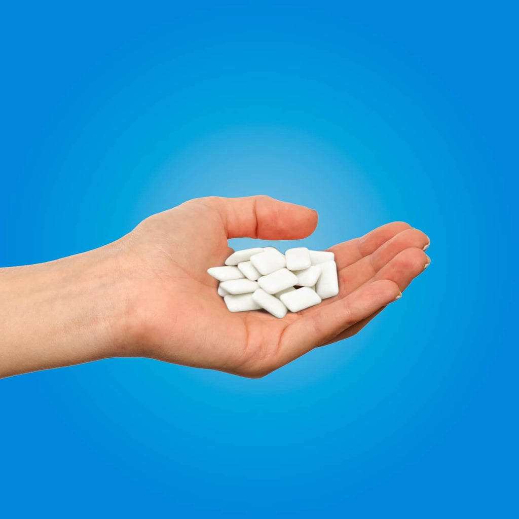 Peppermint gum pieces in a hand, white xylitol-style tablets