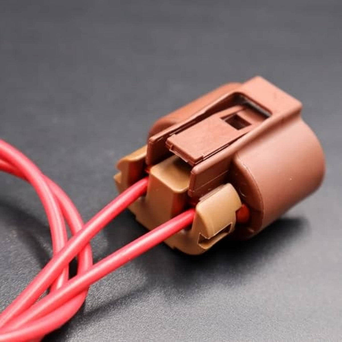 Close-up of brown headlight connector with red wires and locking tab