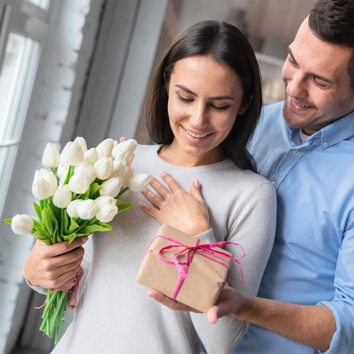 Smiling couple holding a gift box with flowers