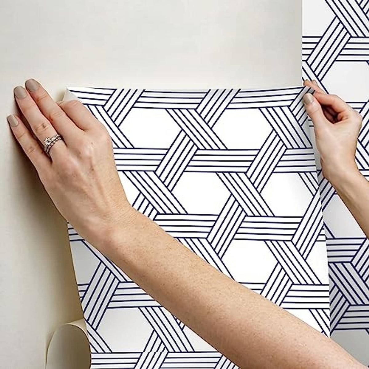 Hands smoothing a blue-and-white geometric lattice wallpaper sheet on wall.