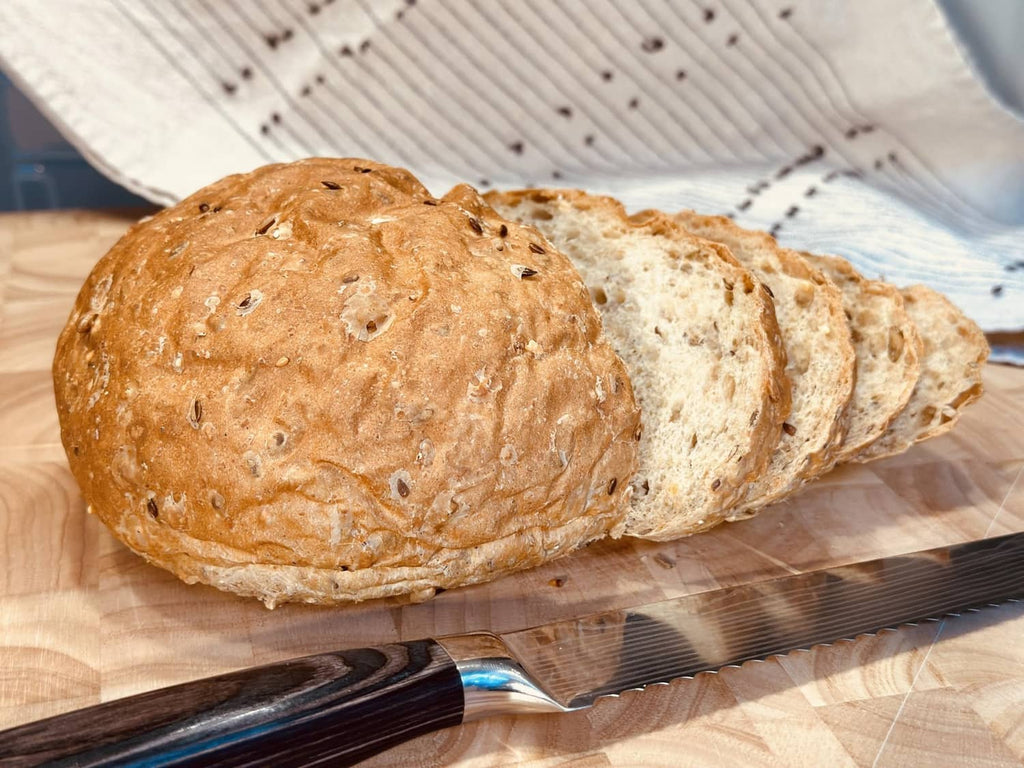 Two 8 grain bread loaves on a tray liner, golden brown seeded crust