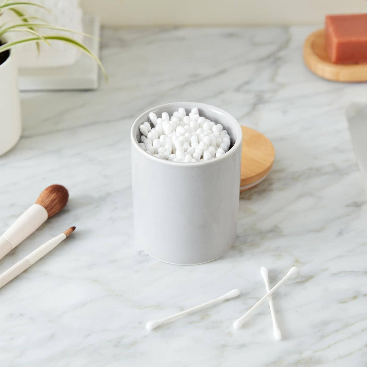 Cotton swabs in a white cup on a countertop, with a few swabs nearby