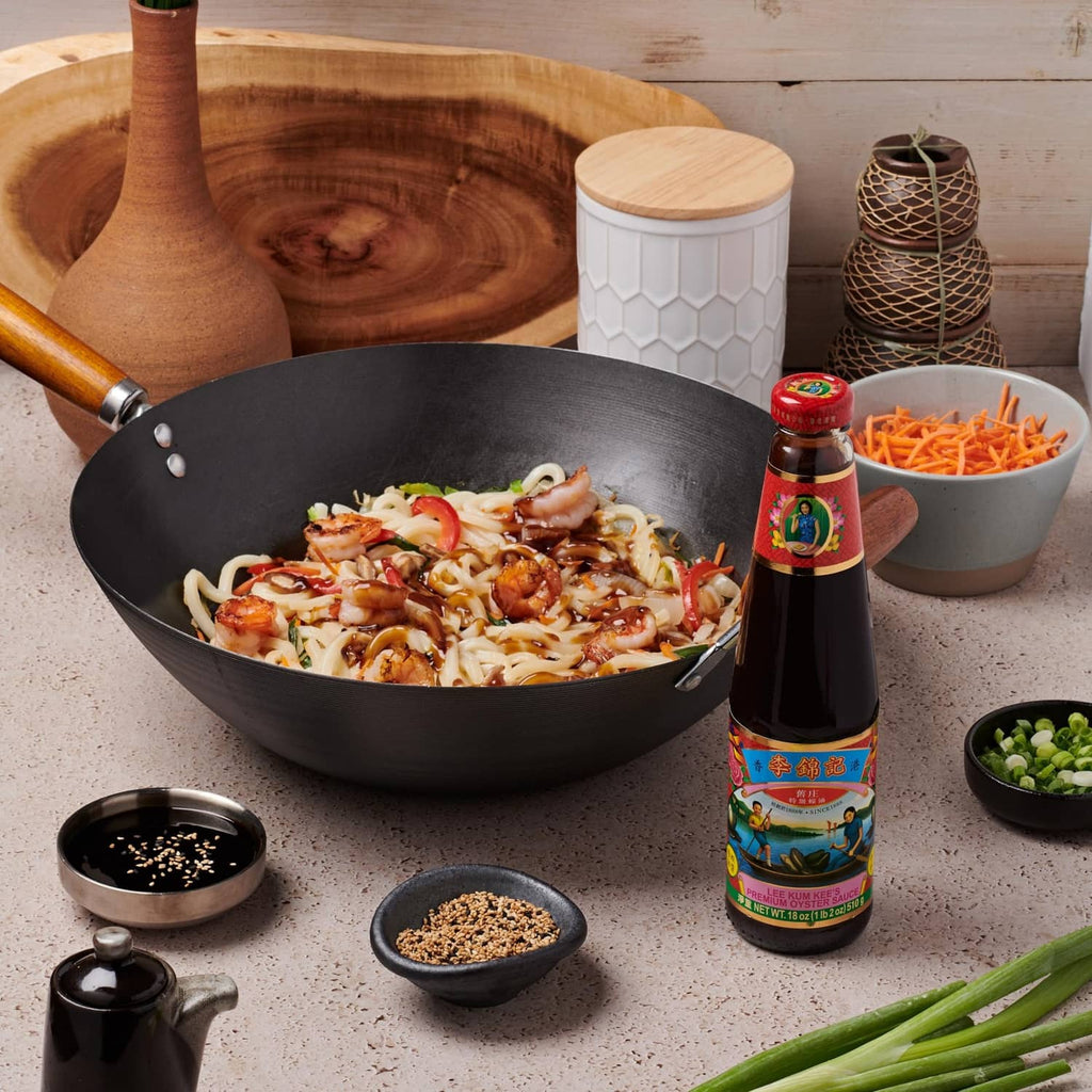 Oyster sauce bottle beside wok with noodles, vegetables, and small condiment bowls
