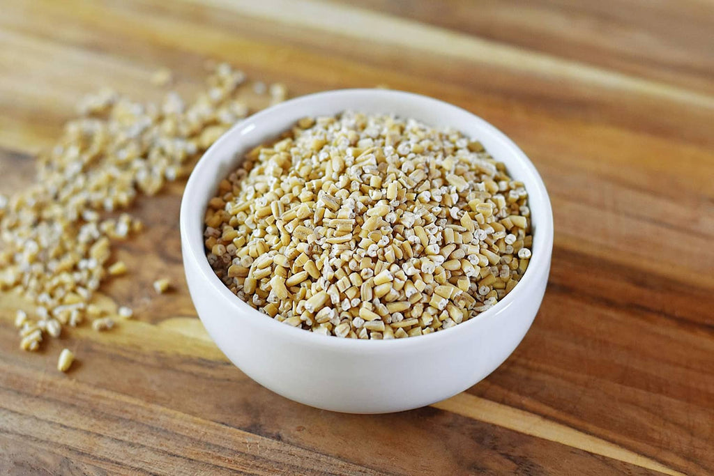 Close-up bowl of steel cut oats with more oats scattered on a wooden surface.