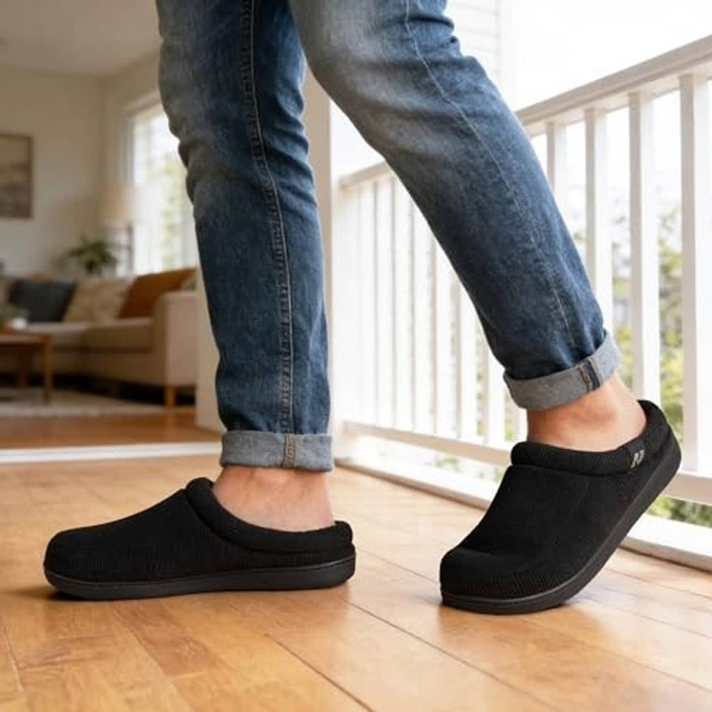 Black corduroy slip-on slippers worn with denim pants, showing rounded toe