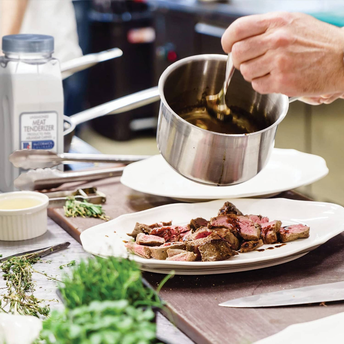 Unseasoned meat tenderizer bottle near a cooking pot and plated meat