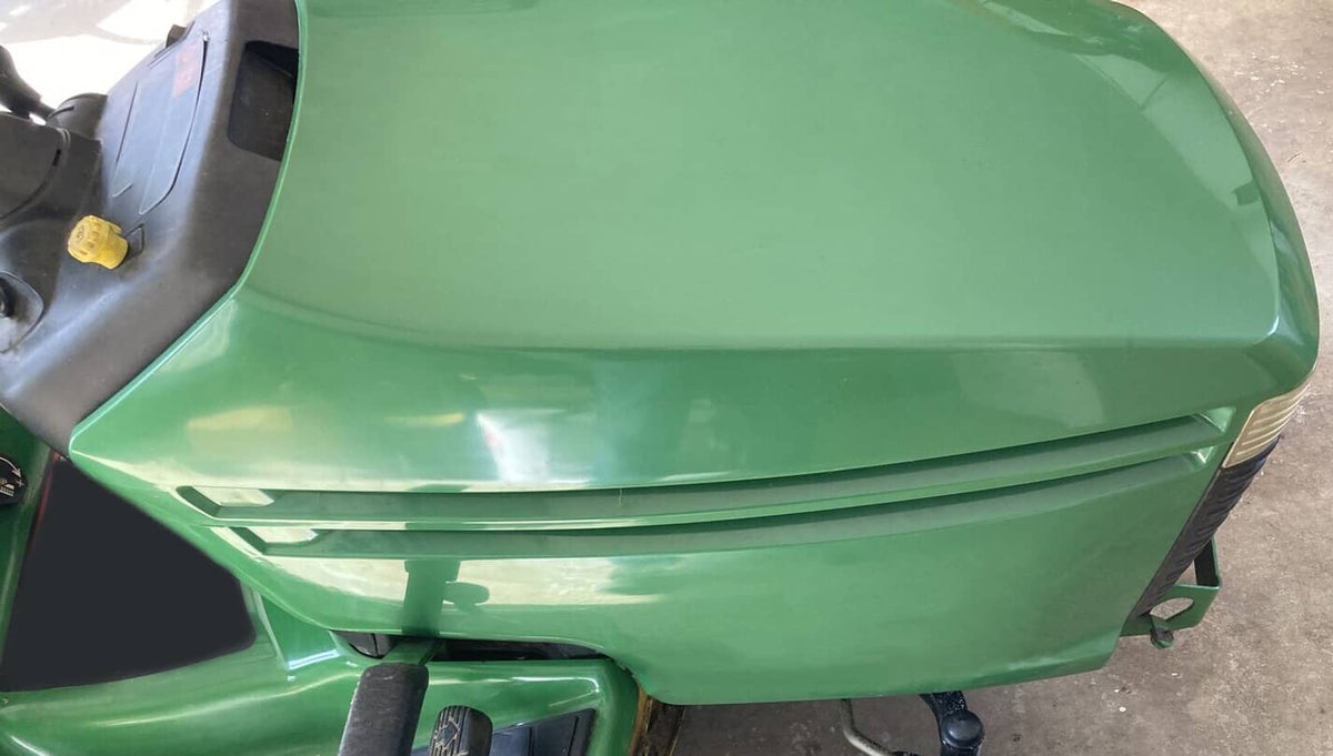 Green mower hood cover installed on riding tractor, close-up