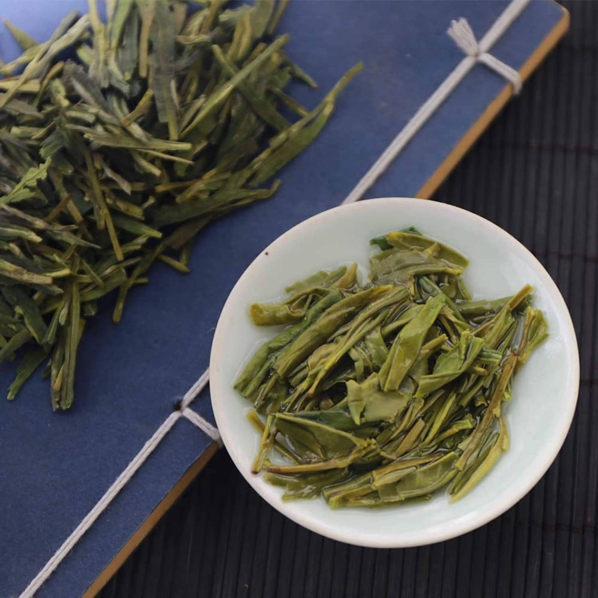 Green tea leaves in white bowl with loose leaves nearby