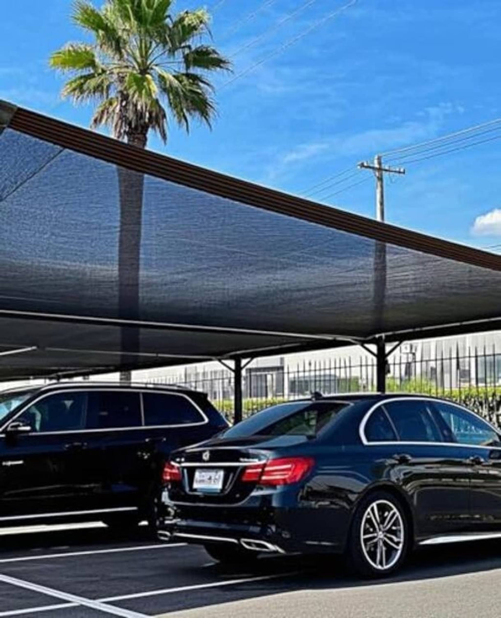 Black shade cloth canopy stretched over a row of cars, with hanging support poles