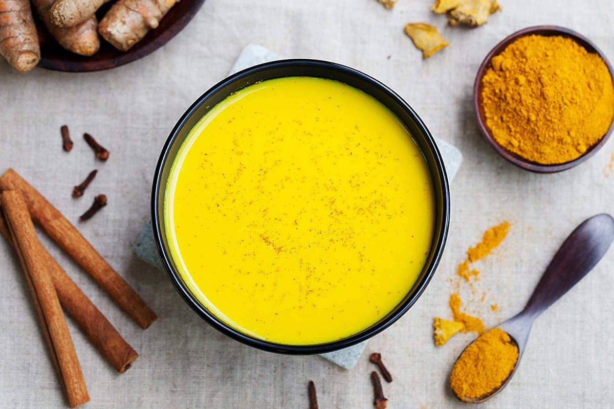 Yellow turmeric latte in a bowl with cinnamon sticks and turmeric spice pieces