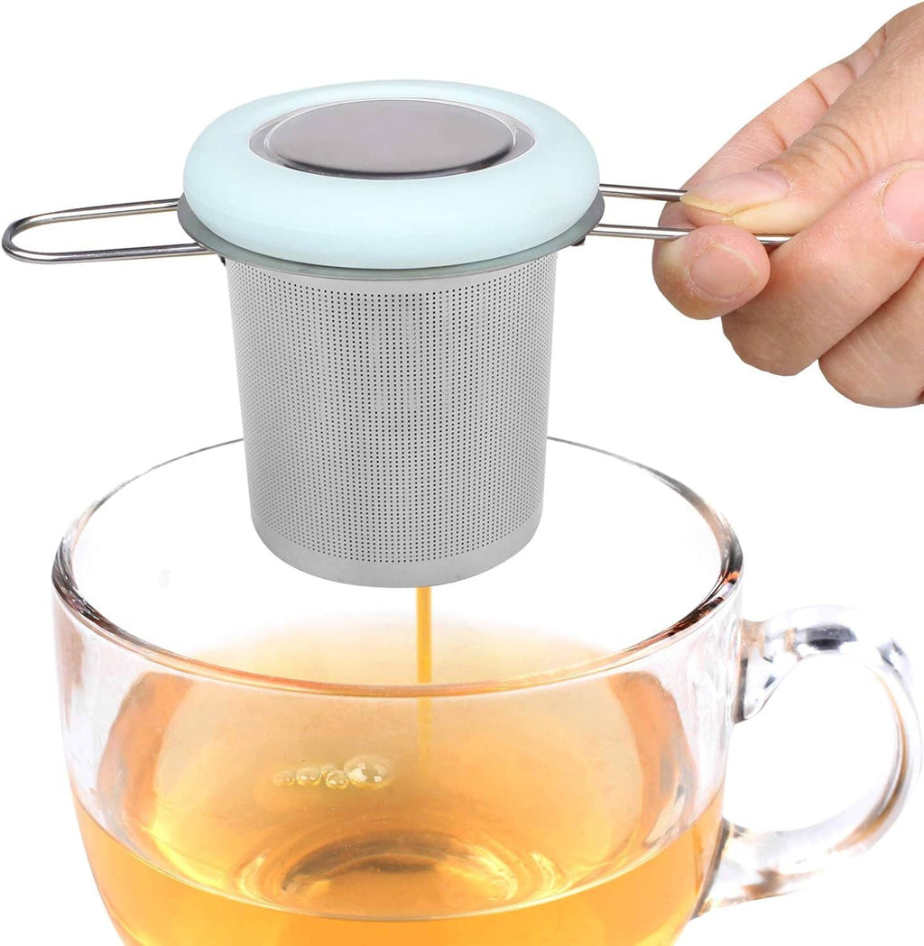Stainless tea strainer with folding handle releasing tea into a glass teapot