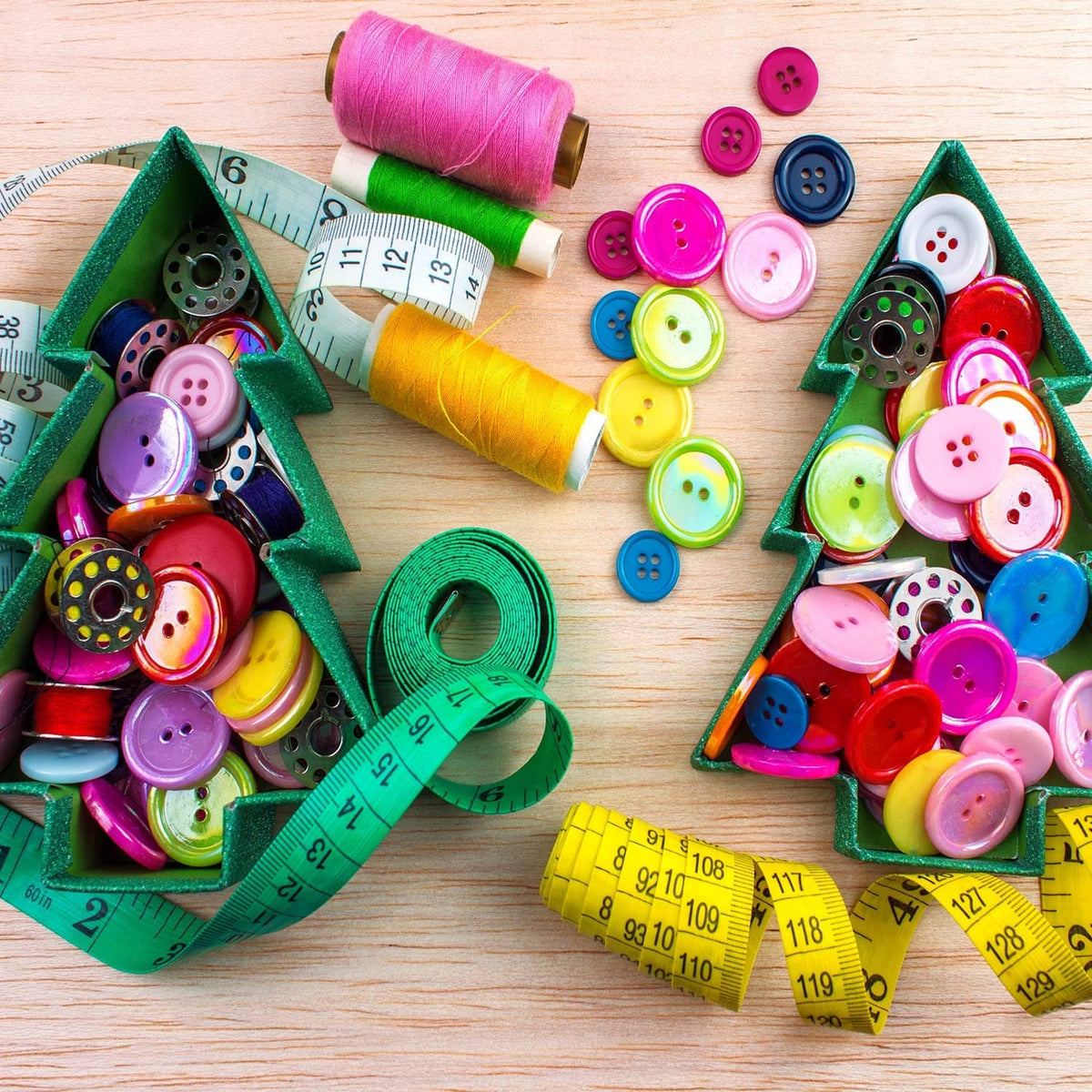 Colorful round resin buttons around thread spools and measuring tape on wood.