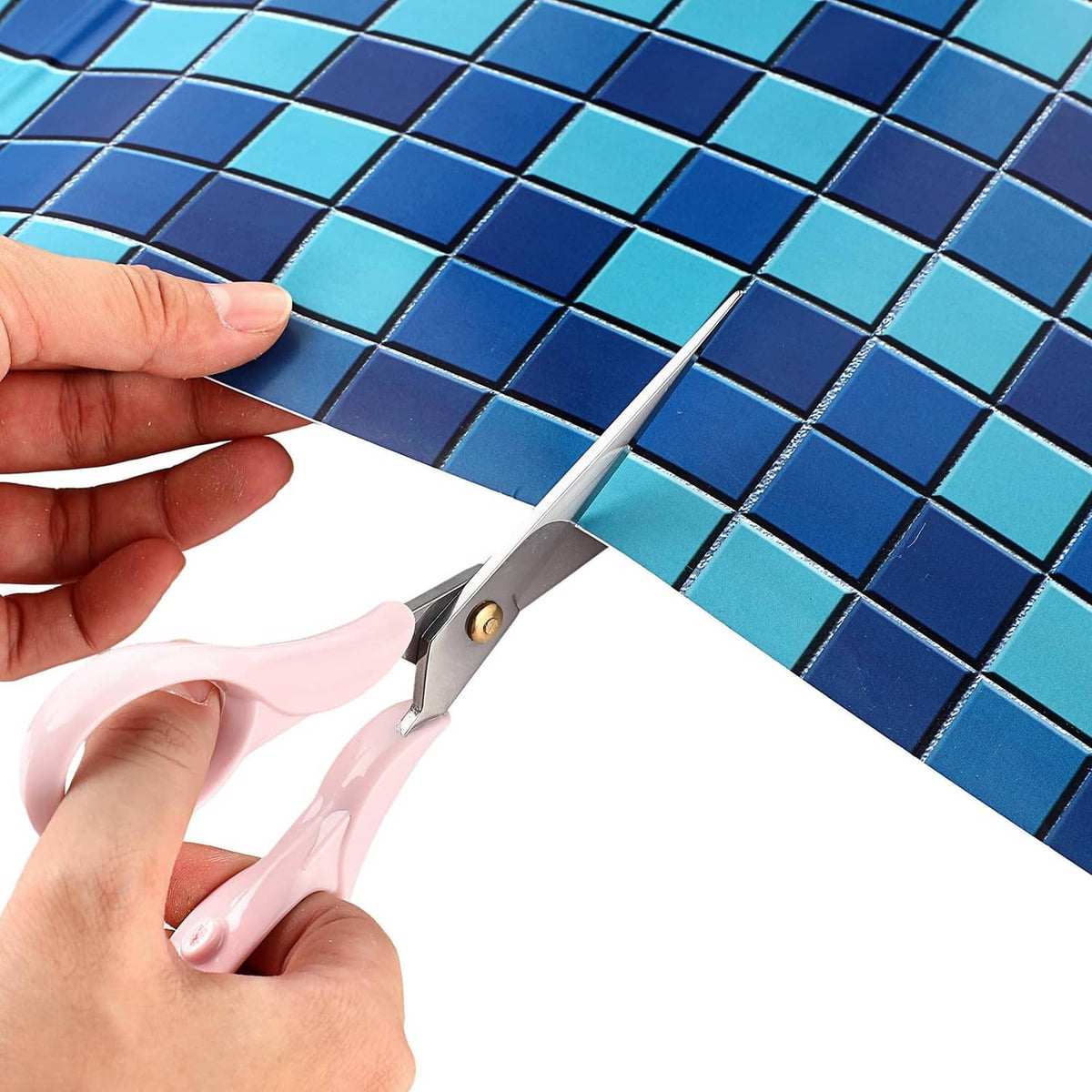 Hand holds blue-green mosaic vinyl patch while trimming with scissors