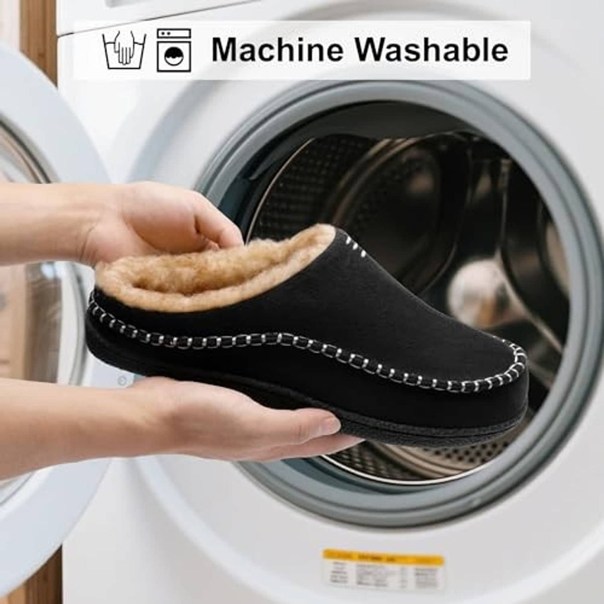 Black slip-on slippers with tan lining, held near a front-loading washing machine.