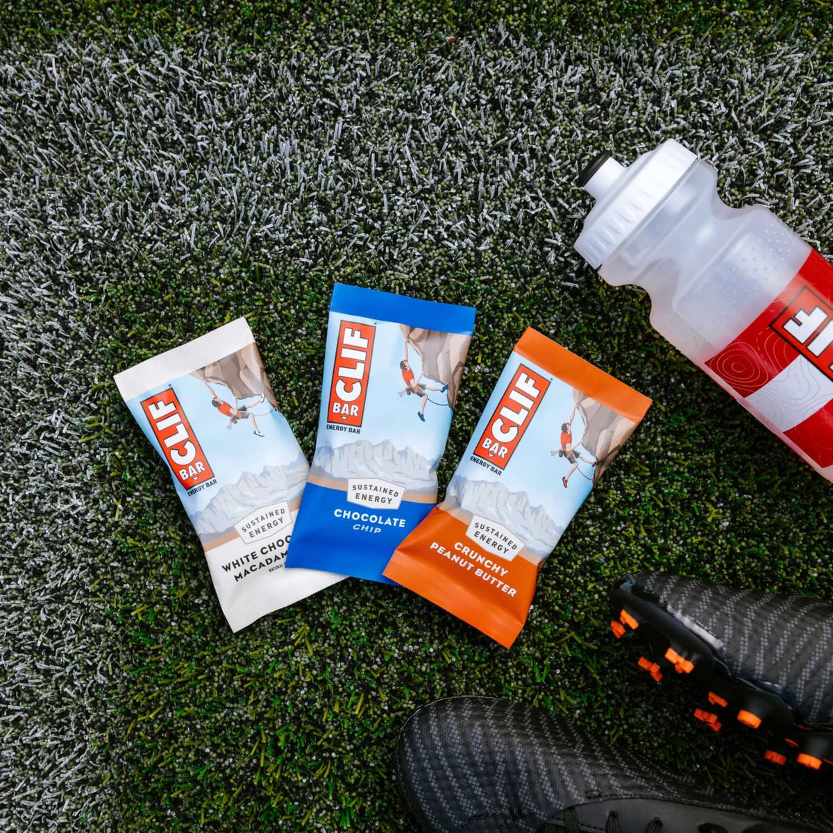 Assorted CLIF BAR energy bar packs on outdoor grass with bottle nearby