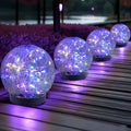 Outdoor solar glass globe lights with glowing purple multicolor LED bulbs on black bases