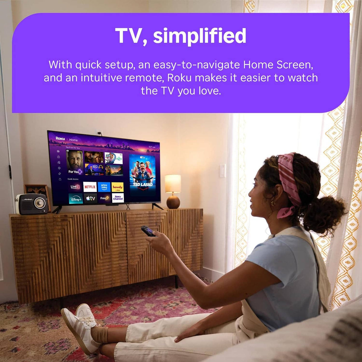 Person holding Roku voice remote facing TV home screen