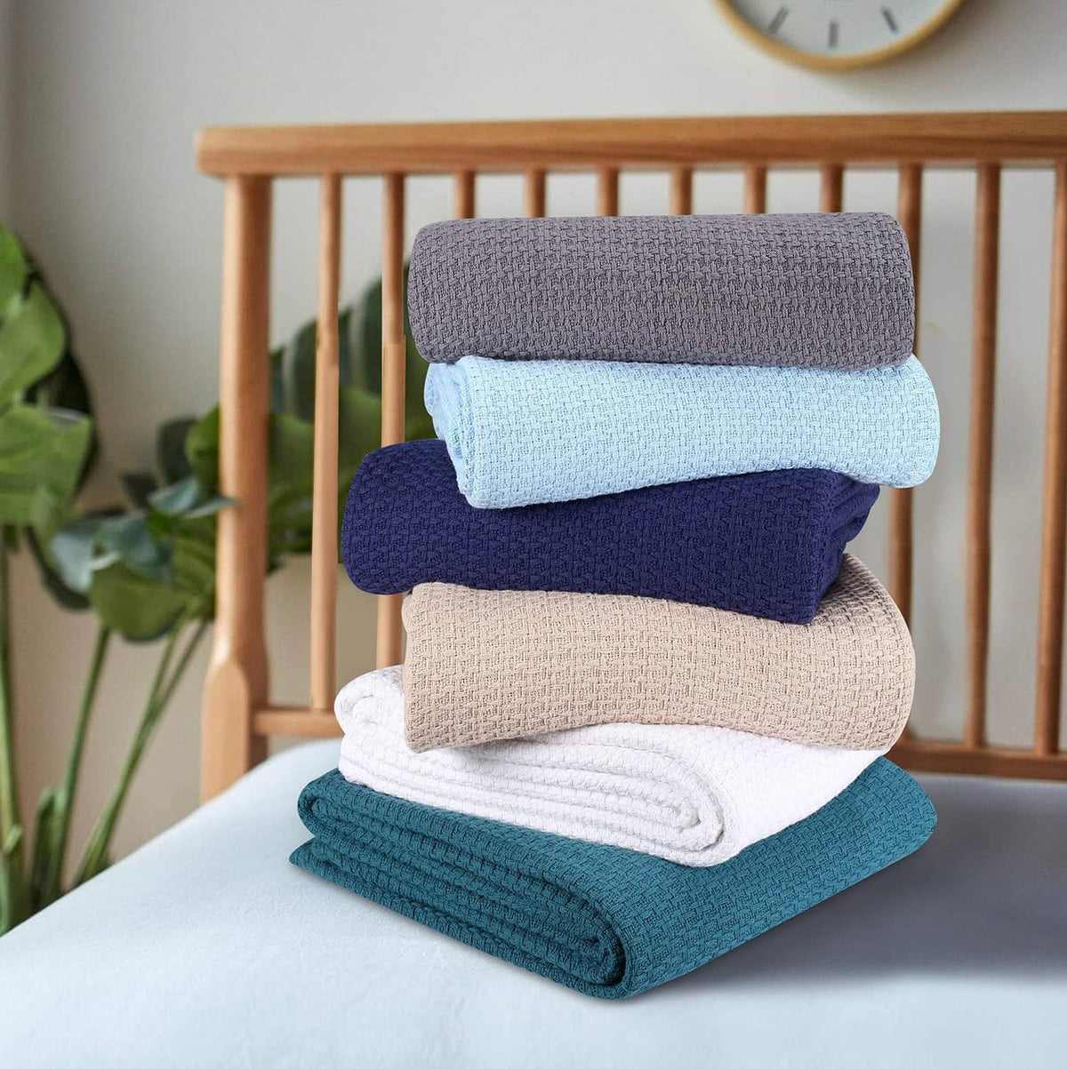 Stack of folded bed blankets in gray, light blue, navy, beige, teal.