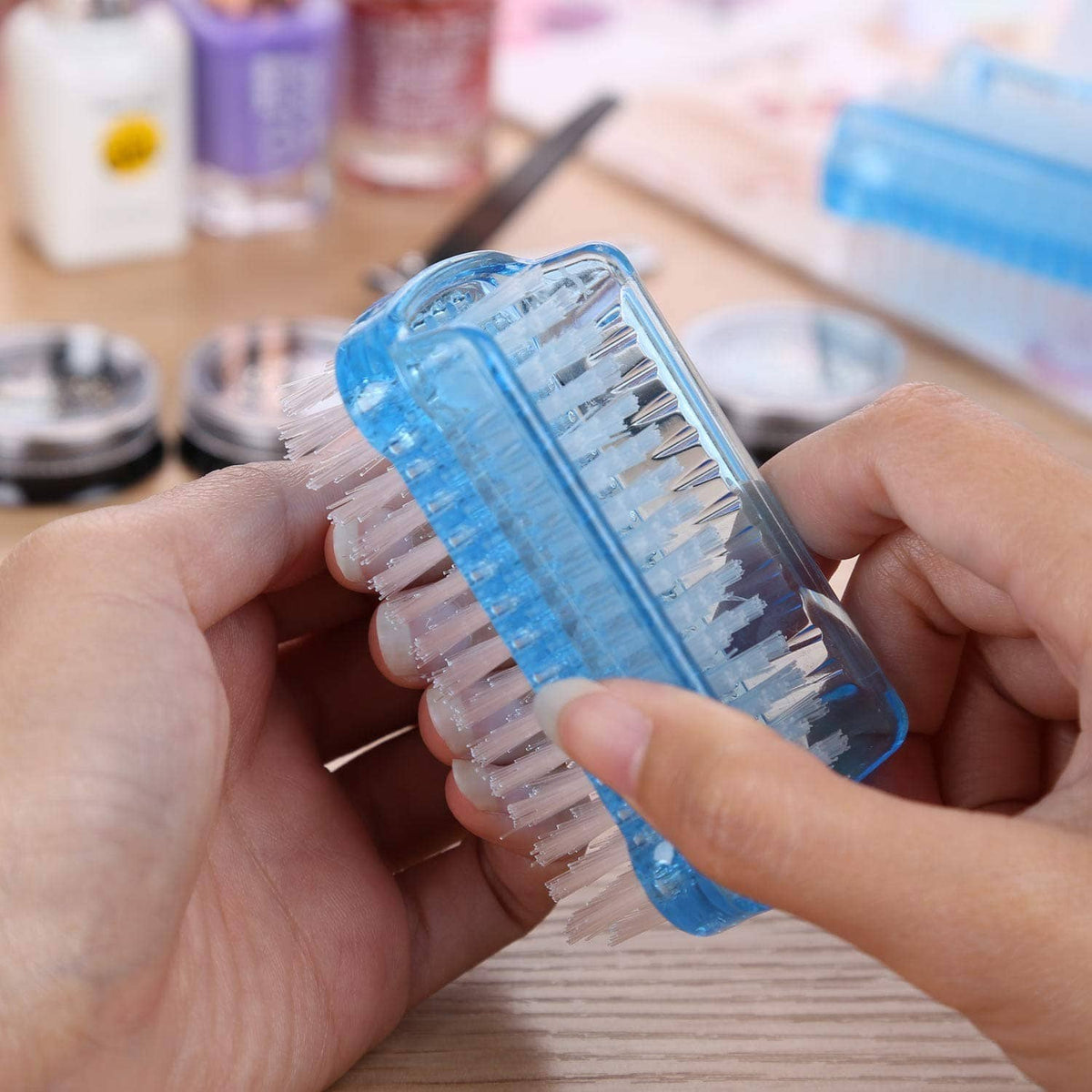 Hand holding dual-sided nail cleaning brush with white bristles and blue holder