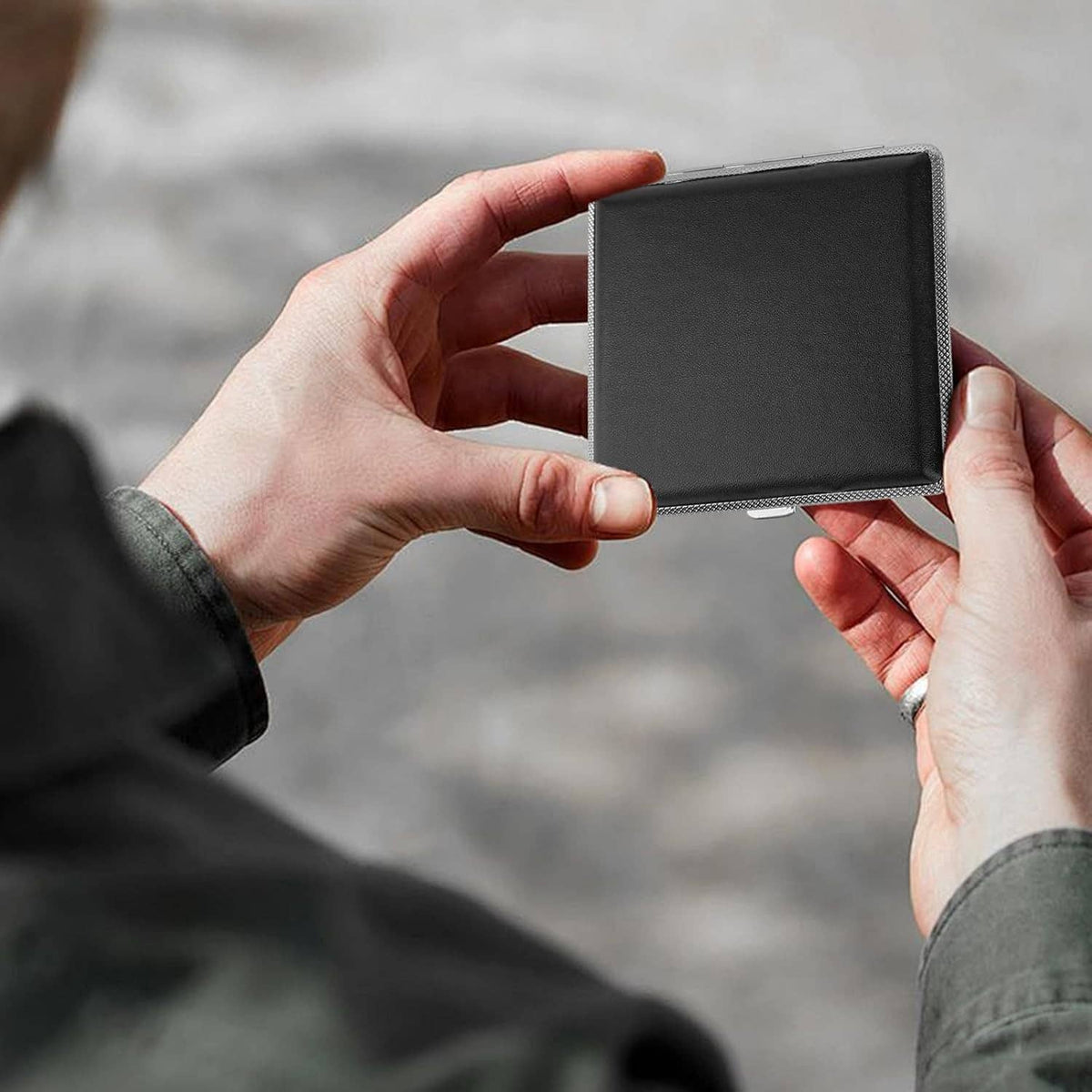 Black slim cigarette case held in hands, thin leather cover with silver textured trim