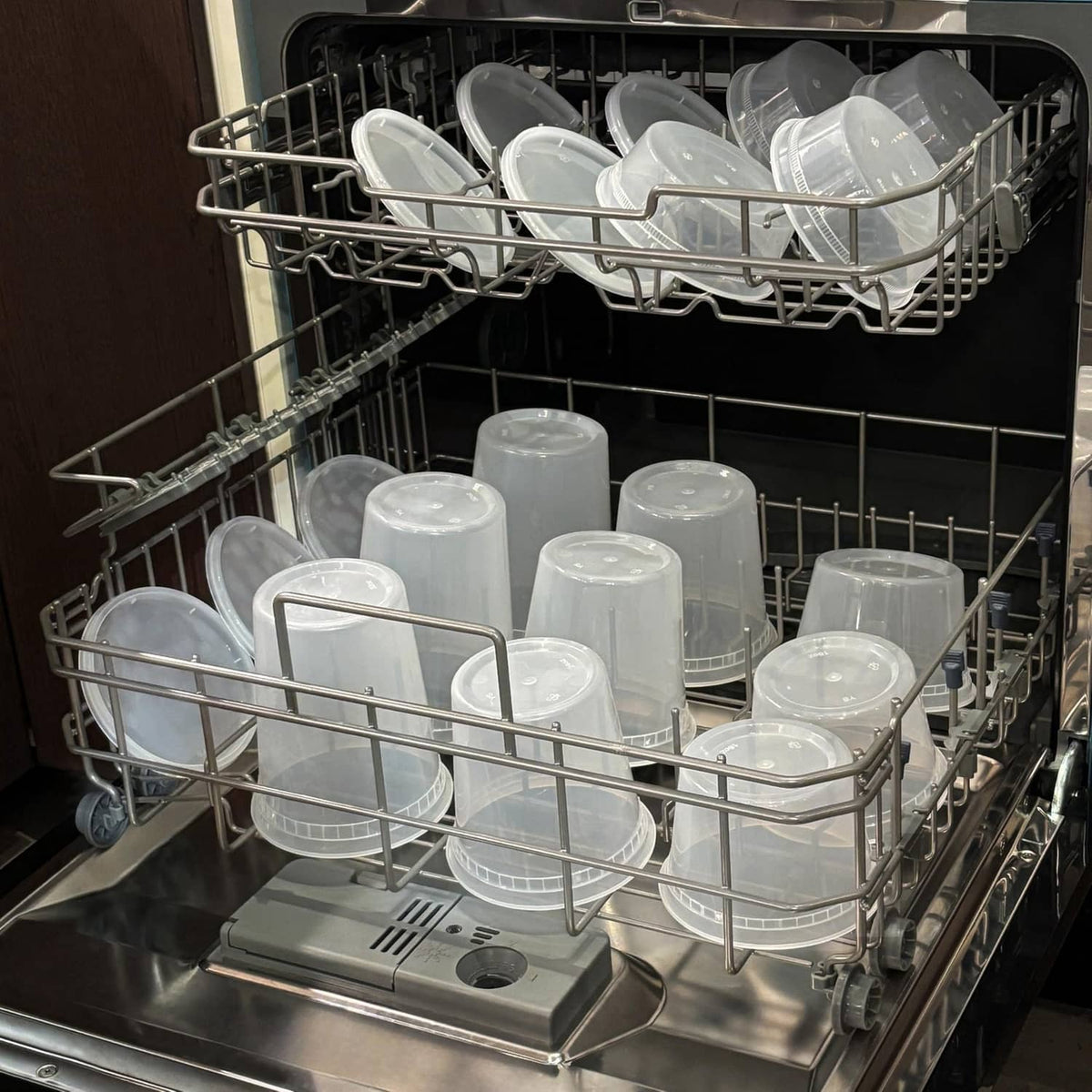Clear plastic deli containers with lids in a dishwasher rack for cleaning