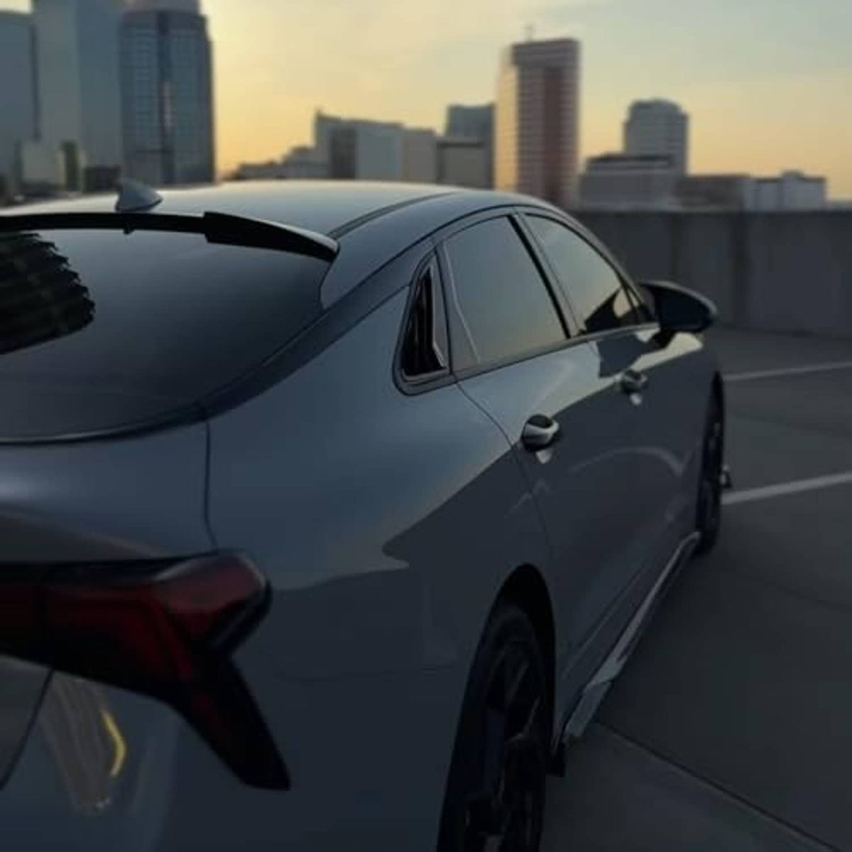 Black roof spoiler wing installed on a dark sedan, rear quarter view.