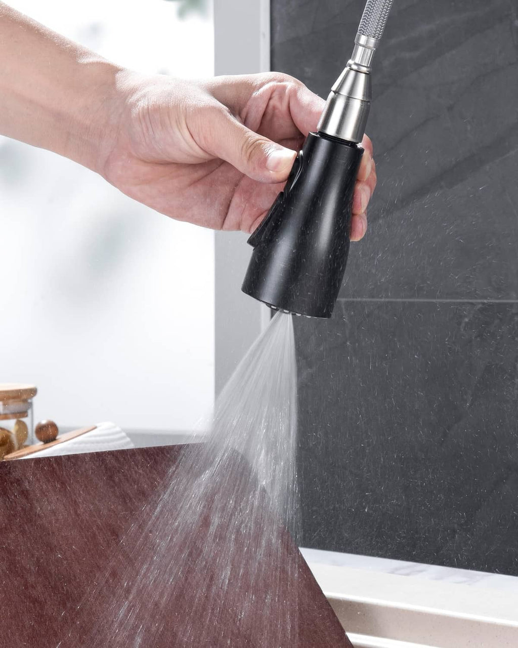 Hand using an oil-rubbed bronze sprayer head producing a strong water stream