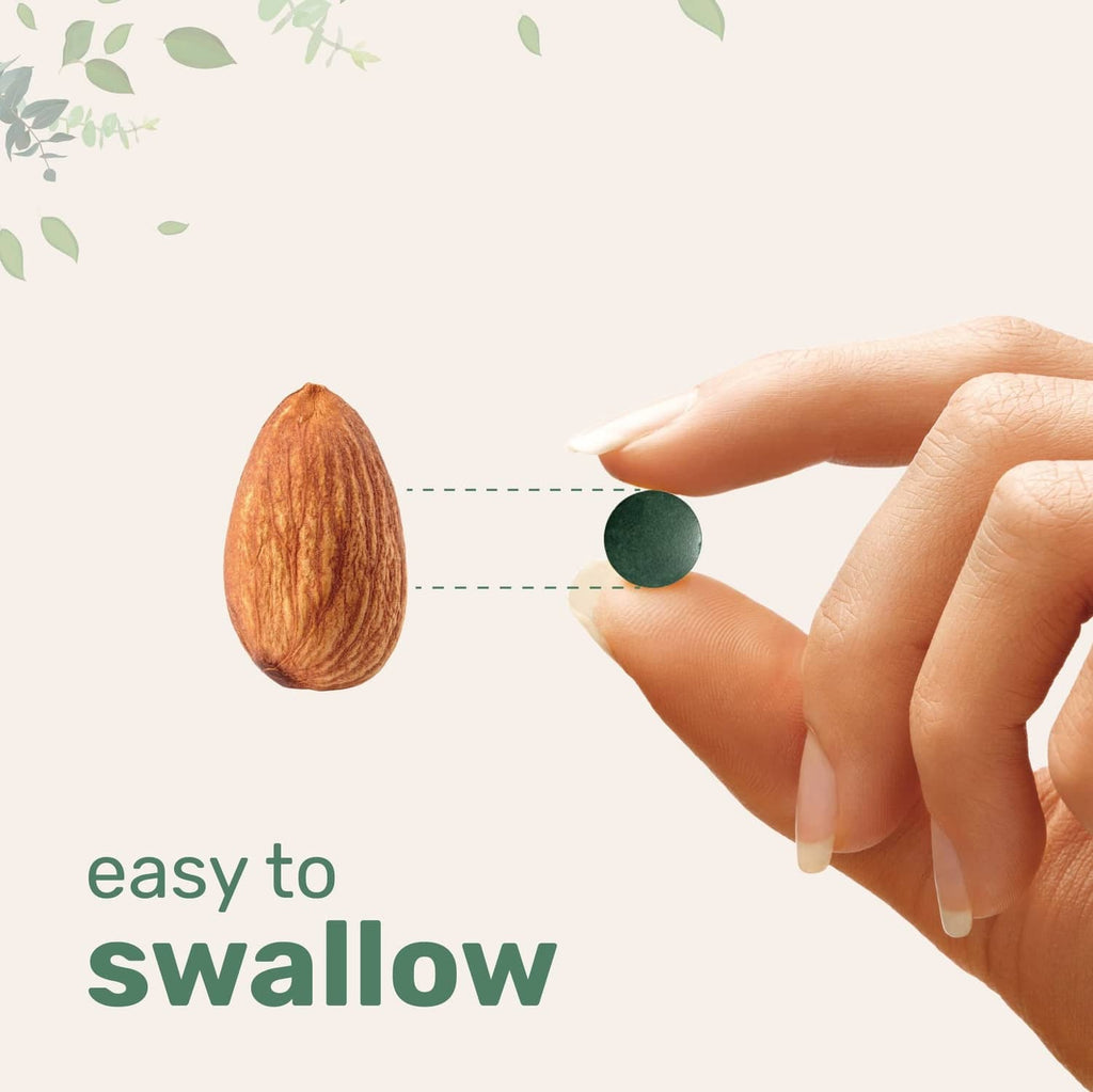 Organic spirulina tablet held in fingers for easy swallowing
