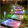 Outdoor solar LED stake lights with multi-color glowing beams along a garden path