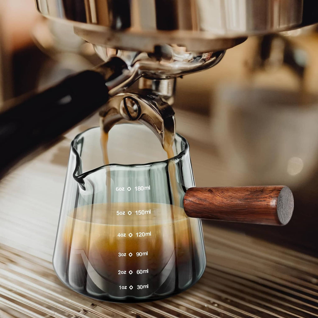 Single-spout clear measuring cup with wood handle pouring coffee, ml markings visible