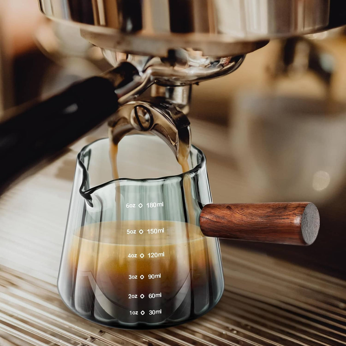 Single-spout clear measuring cup with wood handle pouring coffee, ml markings visible