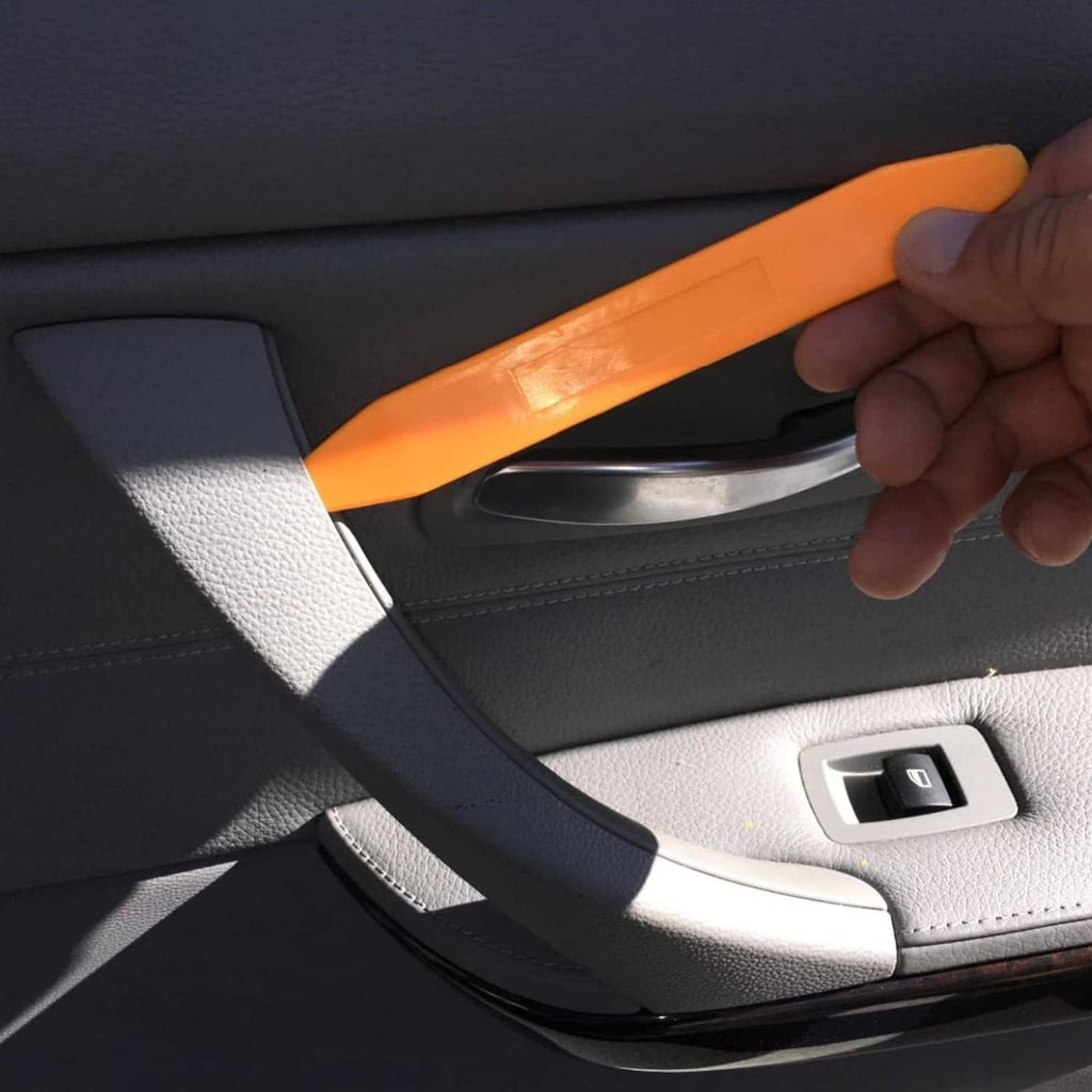 Orange pry tool removing car door panel trim near interior handle