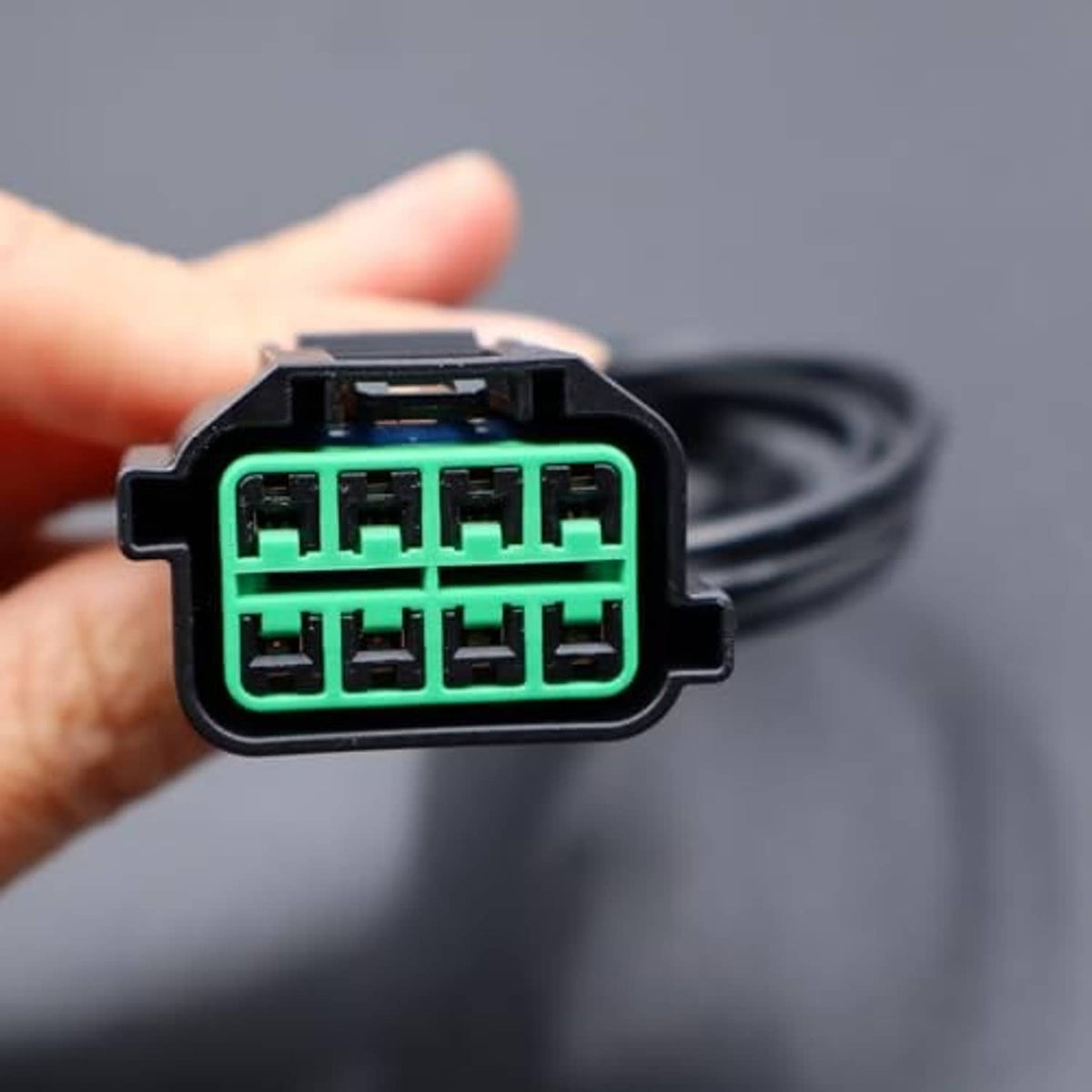 8-way headlight connector plug with green terminal sockets, held in hand