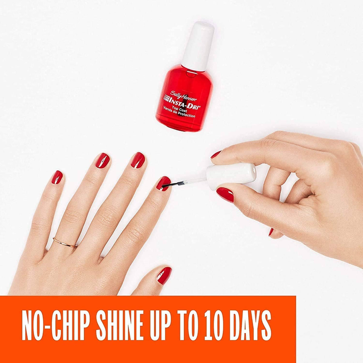 Clear top coat nail bottle while being applied to red manicured nails