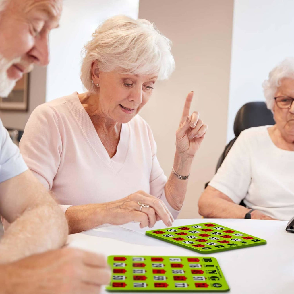 Senior players using green bingo cards with sliding number windows on a table.