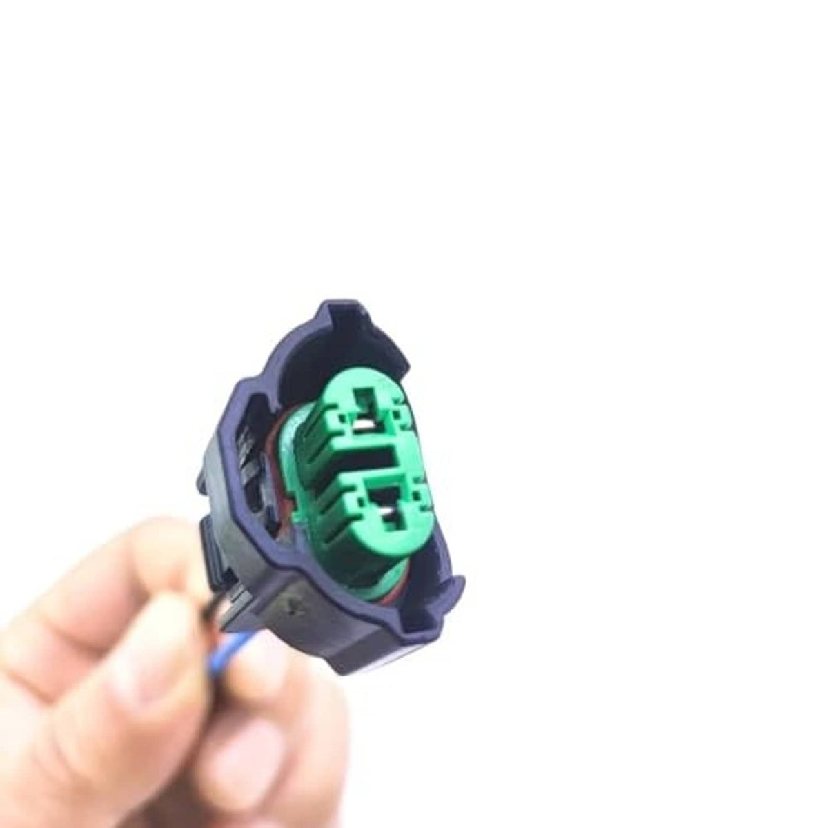 Hand holding headlight bulb female adapter plug with green terminal socket and wires