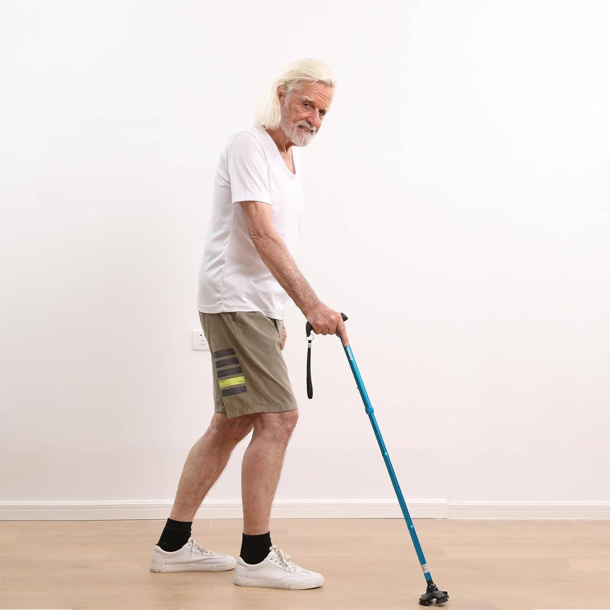 Blue folding walking cane held by an adult, with black ergonomic handle and wrist strap.