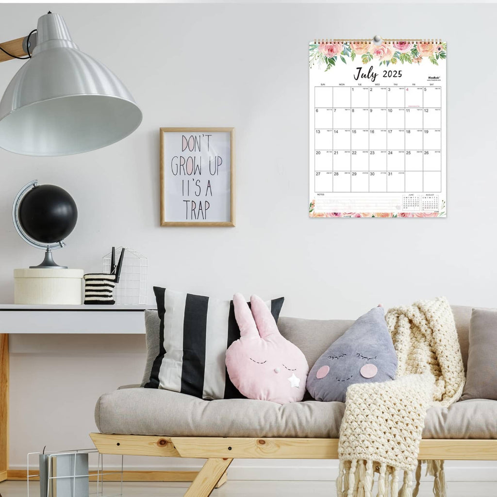 July 2025 monthly wall calendar with spiral binding displayed on a living room sofa