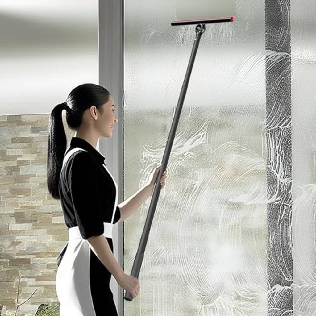 Window squeegee with long black handle and red-edged blade removing water from glass