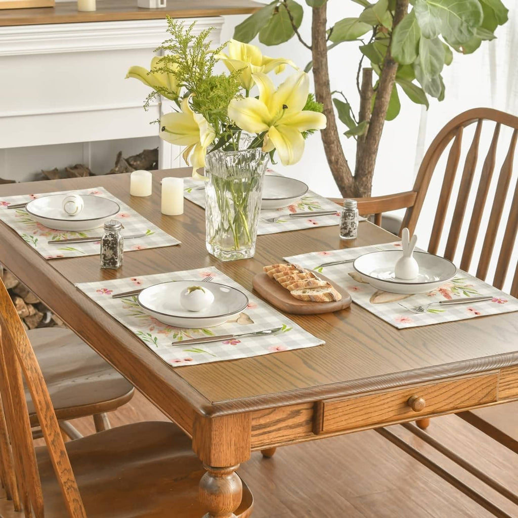 Rectangular beige plaid bunny-ear floral placemats on a wooden dining table.