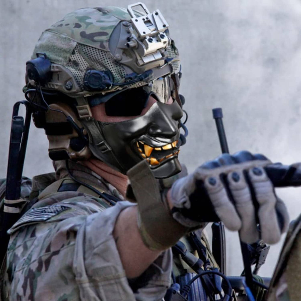 Black half-face demon mask with gold teeth worn by person in tactical gear