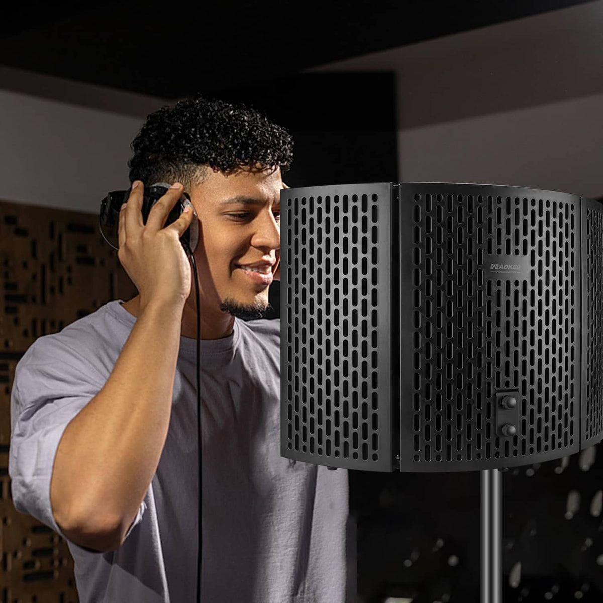 Microphone isolation shield with perforated black panels beside a studio user