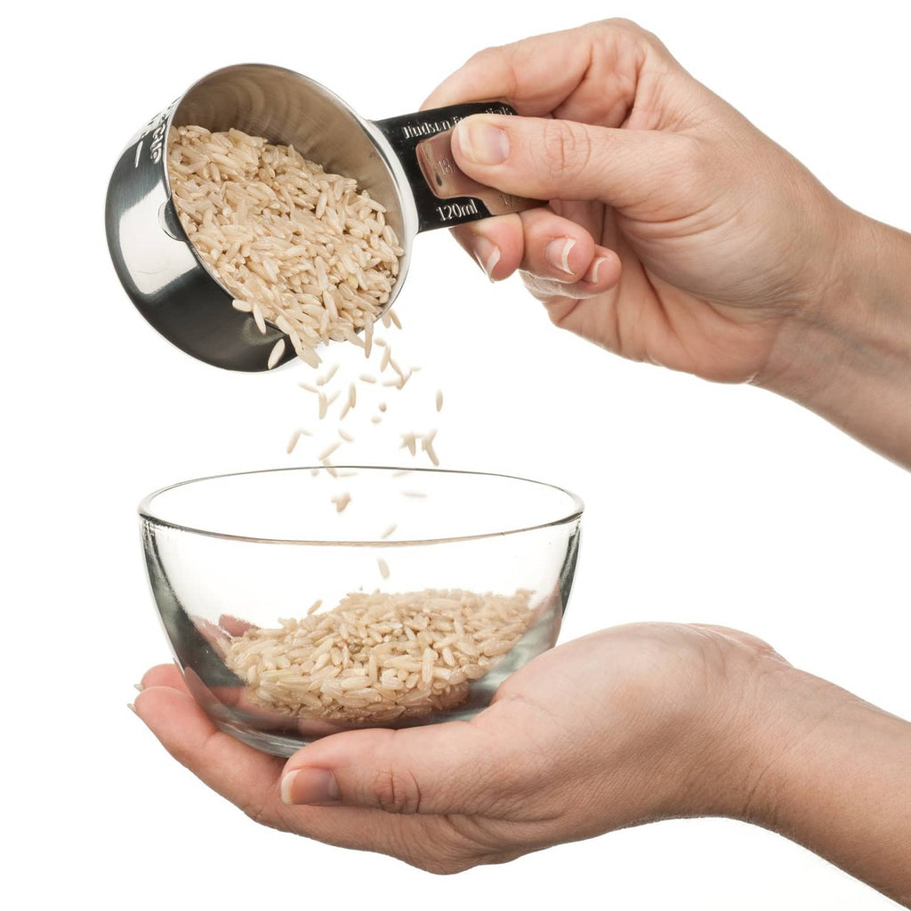 Hand pouring grain from a stainless steel measuring cup into a glass bowl