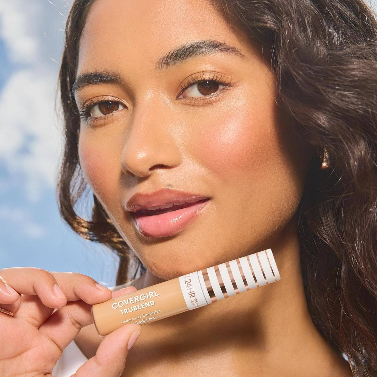 Concealer tube held near face, matte full-coverage look on natural complexion
