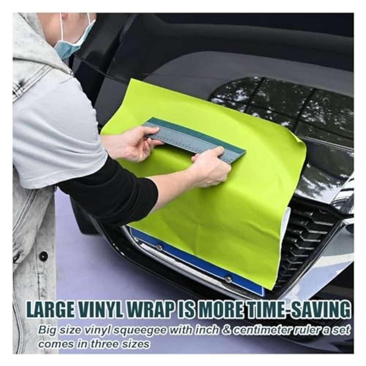 Person applying vinyl wrap using a gray squeegee with ruler on a car window