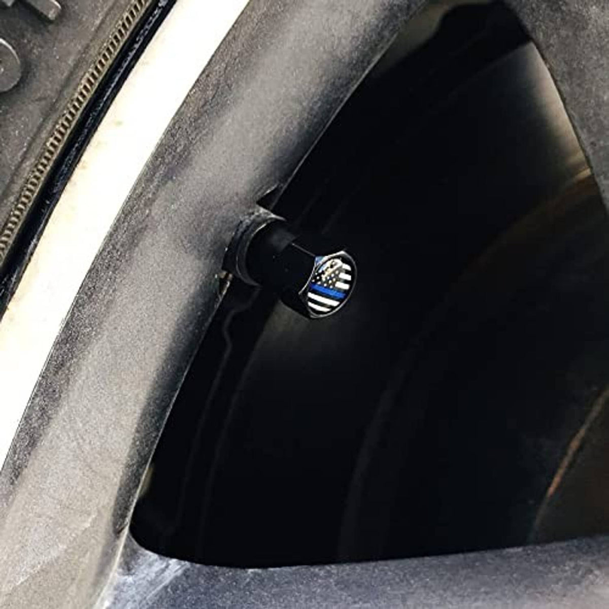 Black tire valve stem cap with thin blue line flag emblem installed on a wheel