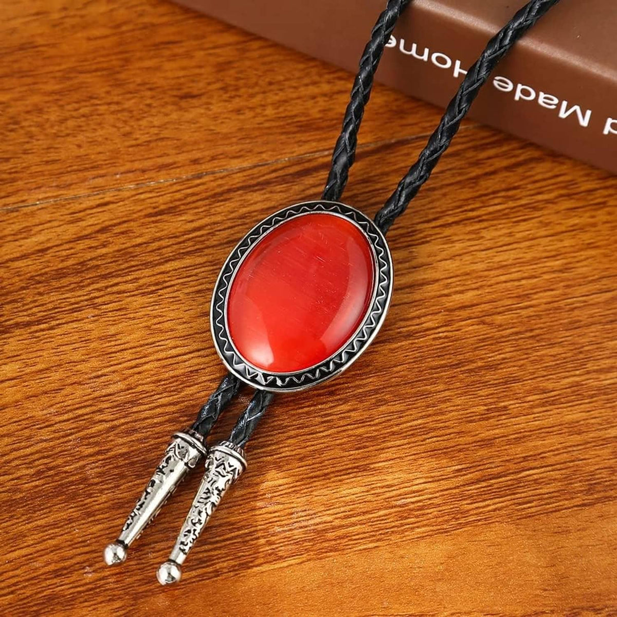 Bolo tie pendant on wood: black cord with red oval stone and engraved silver tips