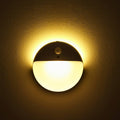 Round wall motion sensor night light, emitting warm yellow light.