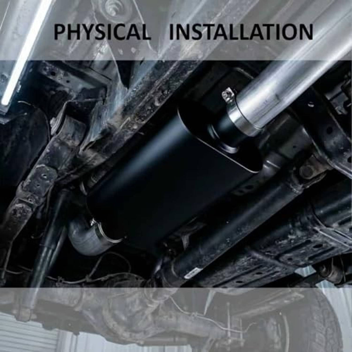 Black exhaust muffler installed under vehicle, with connected inlet and outlet pipes.